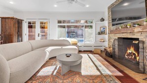 Una sala de estar moderna con un sofá modular, una mesa de centro redonda, una chimenea y un televisor grande montado en una pared de ladrillo.