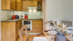 Una cocina moderna con armarios de madera, electrodomésticos de acero inoxidable y un comedor con una mesa dispuesta para dos personas.