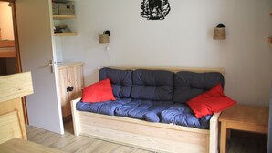Una habitación acogedora con un sofá de madera, dos almohadas rojas, una lámpara de pared y un estante con cestas.