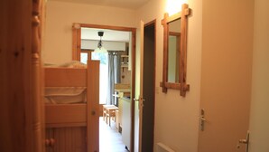 Un estrecho pasillo con una litera, una puerta que da a una cocina y un espejo en la pared.