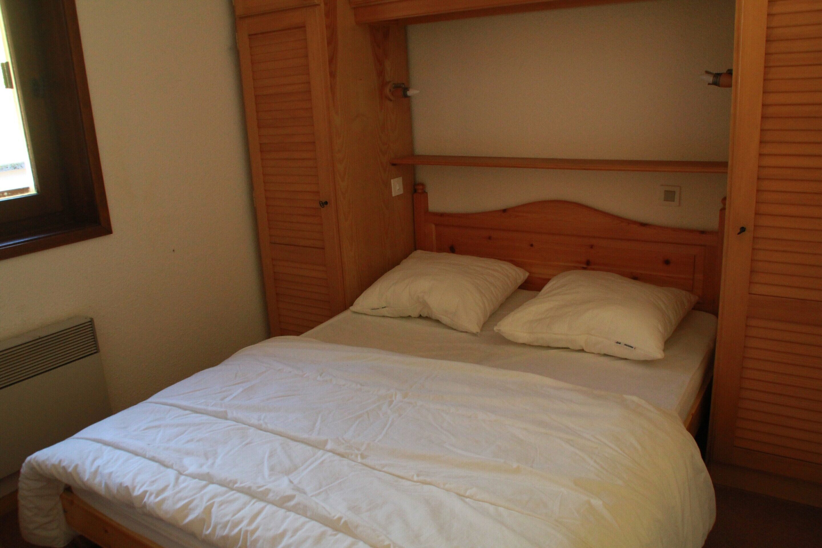 A single bed with white bedding in a room with wooden walls and a window.