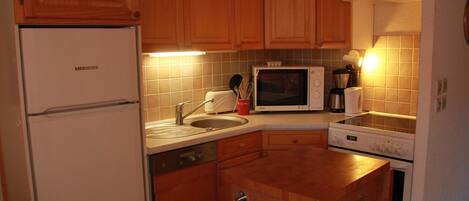 A compact kitchen with wooden cabinets, a built-in microwave, a sink, and a stove.