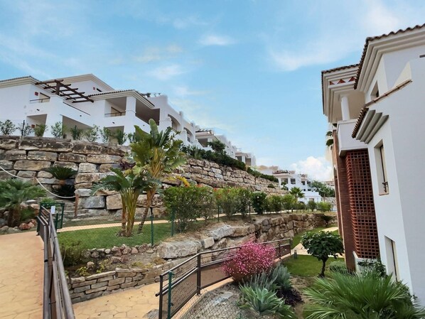 A residential area with white buildings, a stone retaining wall, and various plants.