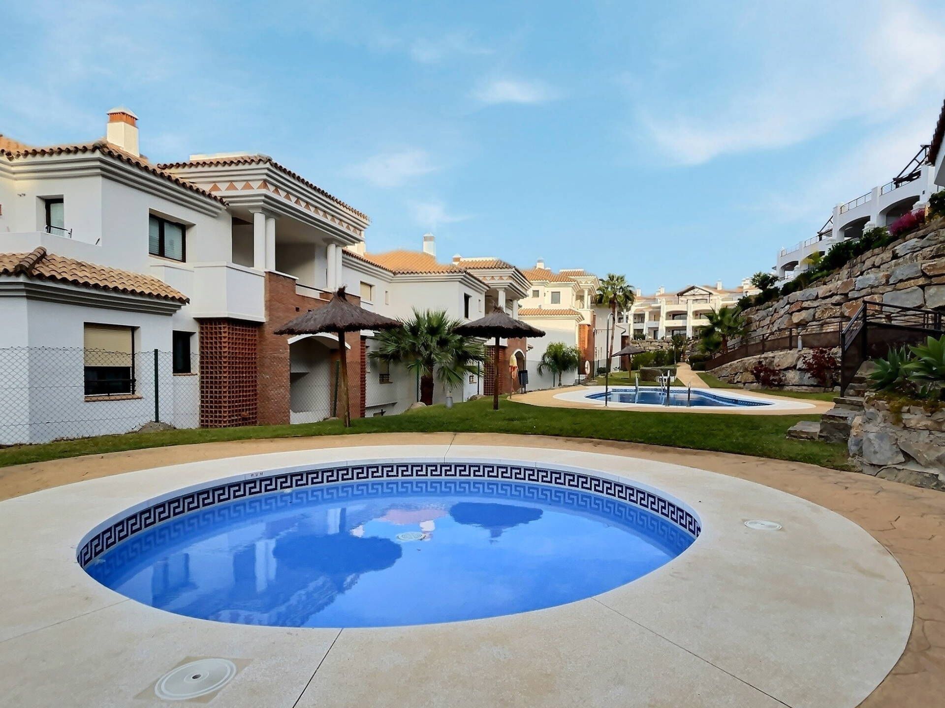 A swimming pool with a decorative edge, surrounded by a well-maintained lawn and a building with a tiled roof.