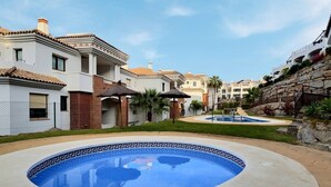 Una piscina con un borde decorativo, rodeada por un césped cuidado y un edificio con tejado de baldosas.