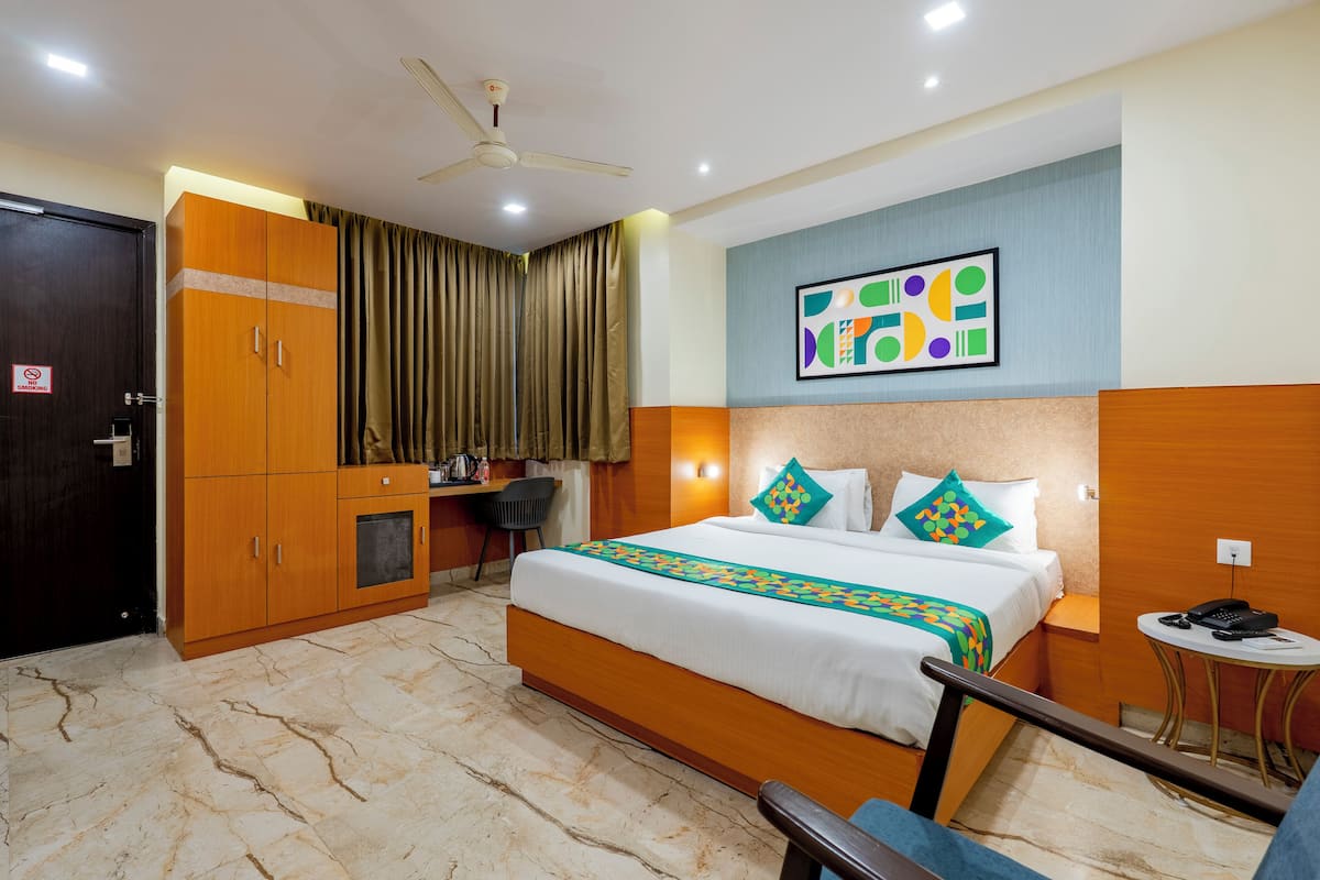 A hotel room with a bed, a desk, a chair, a wardrobe, and a ceiling fan.