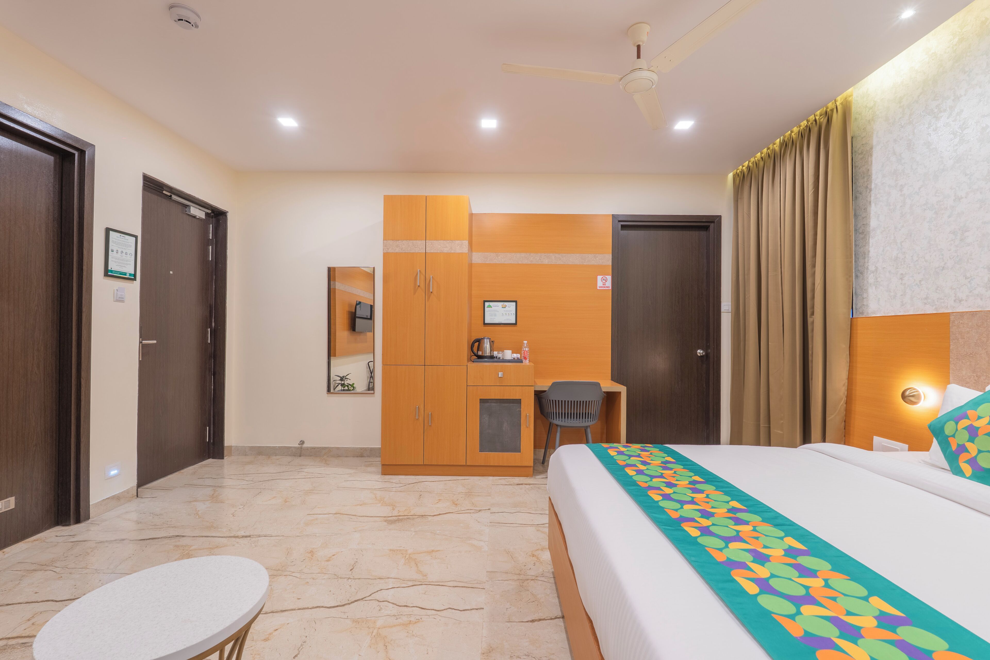 A hotel room with a bed, a desk, a chair, a small table, and a wardrobe.