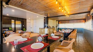 Un restaurant avec une longue table à manger, plusieurs chaises et un espace cuisine à l’arrière-plan.