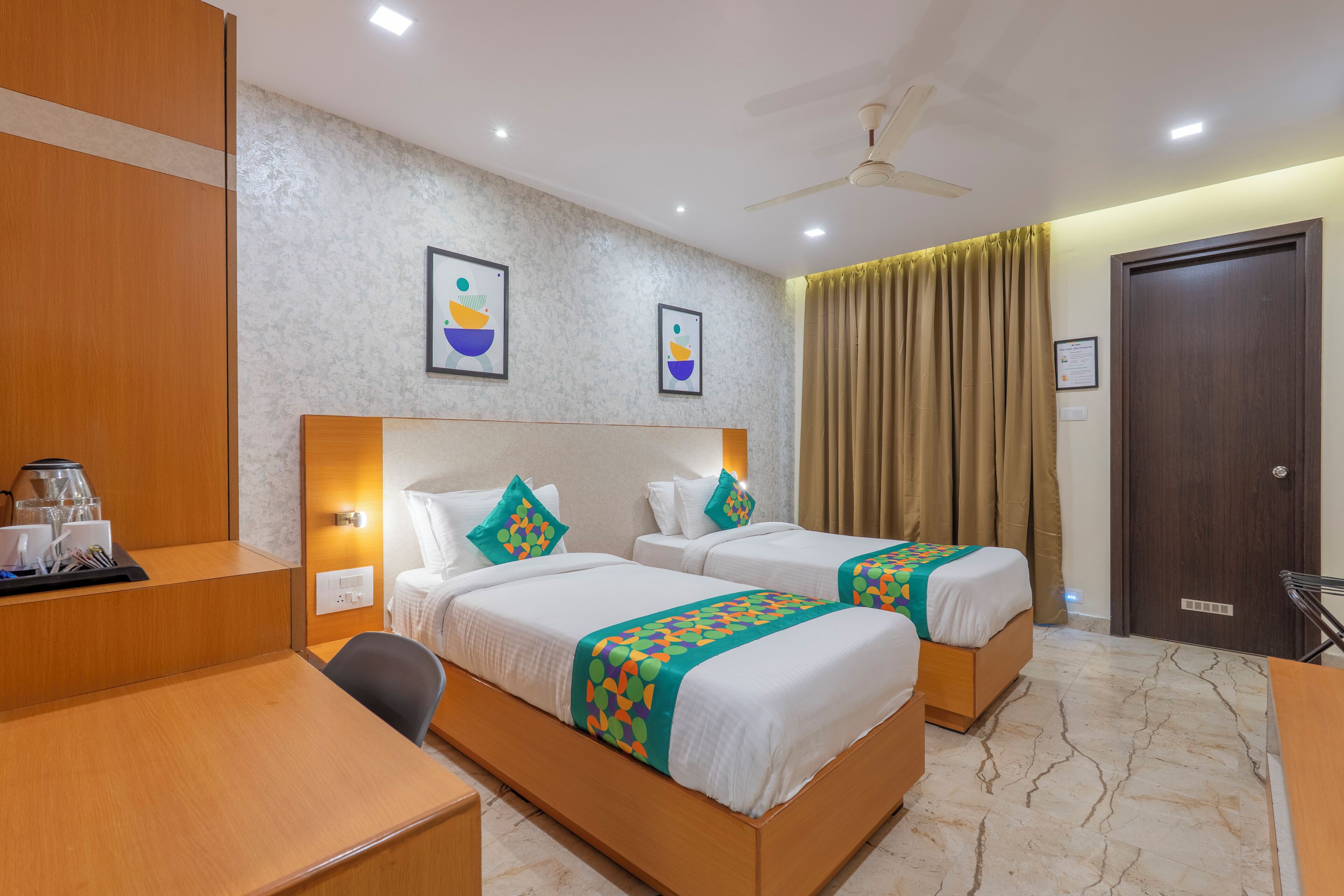 A hotel room with two beds, a desk, a chair, a coffee station, and a ceiling fan.