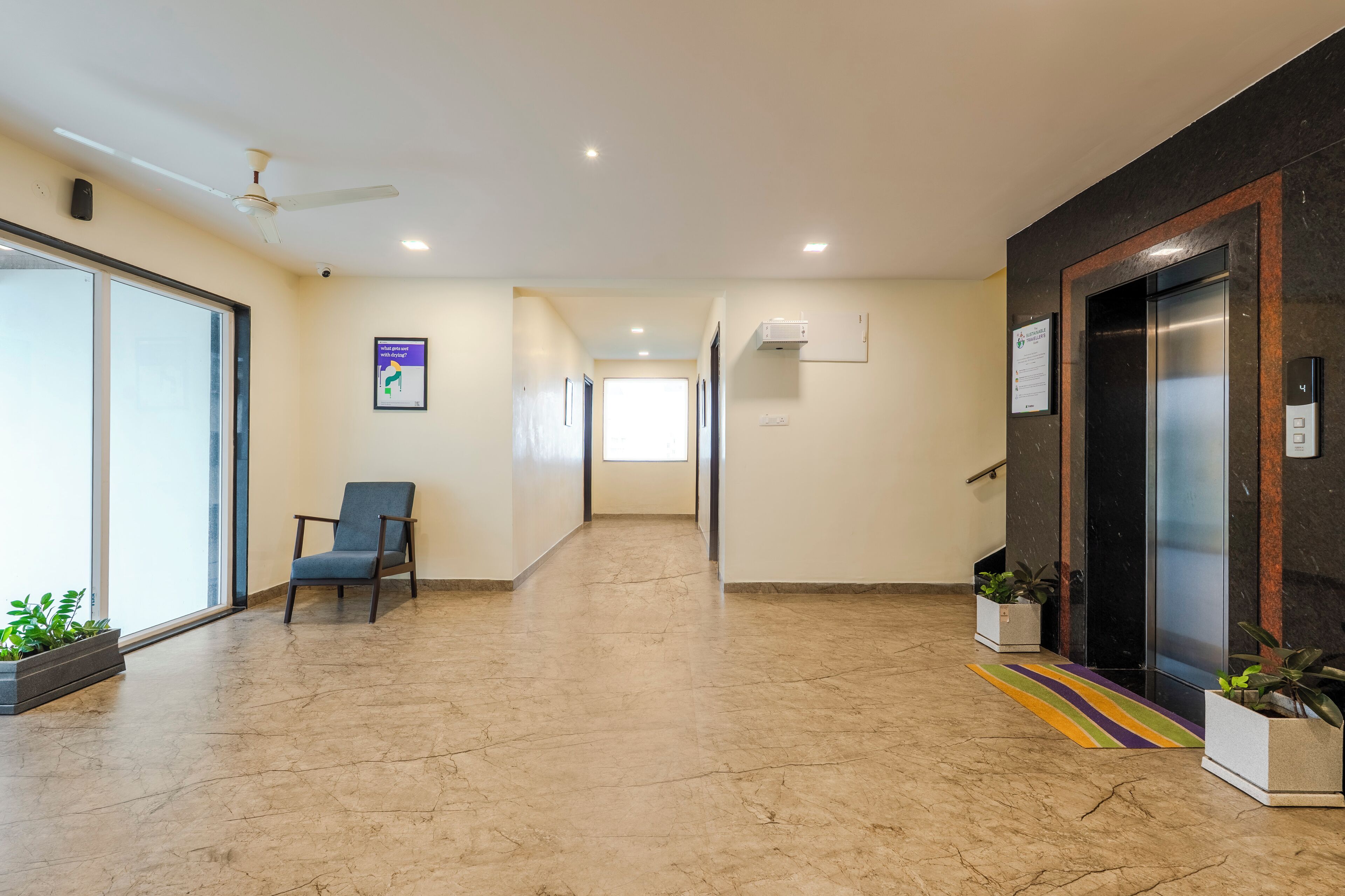 A spacious hallway with a ceiling fan, a chair, potted plants, an elevator, and a colorful rug.