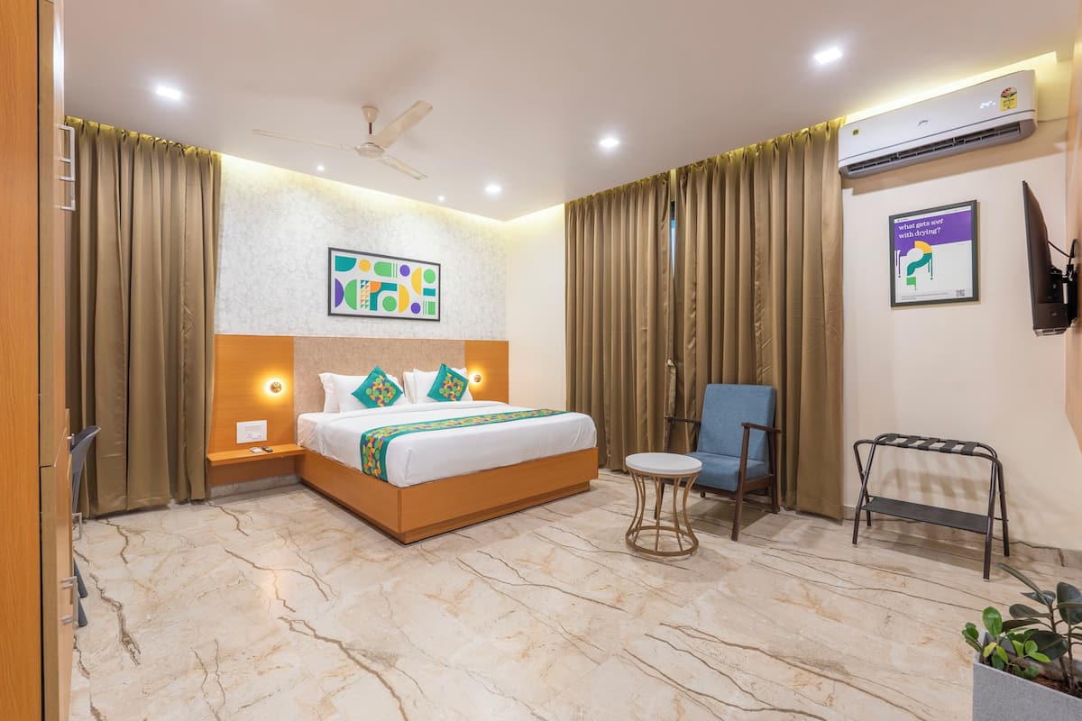 A hotel room with a bed, a chair, a small table, an air conditioning unit, and a TV mounted on the wall.
