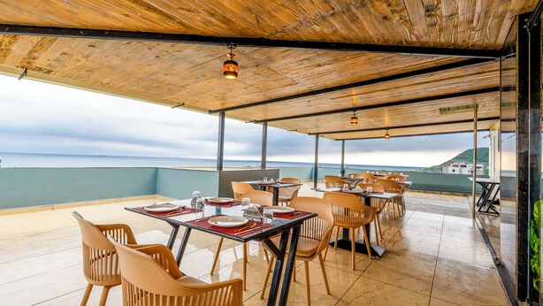 Un espace de restauration en plein air avec des tables et des chaises, un plafond en bois et une vue sur la mer.
