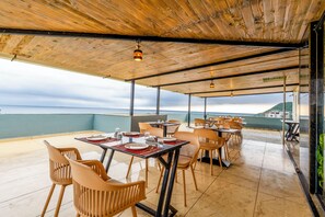 Een terras met tafels en stoelen, een houten plafond en uitzicht op zee.