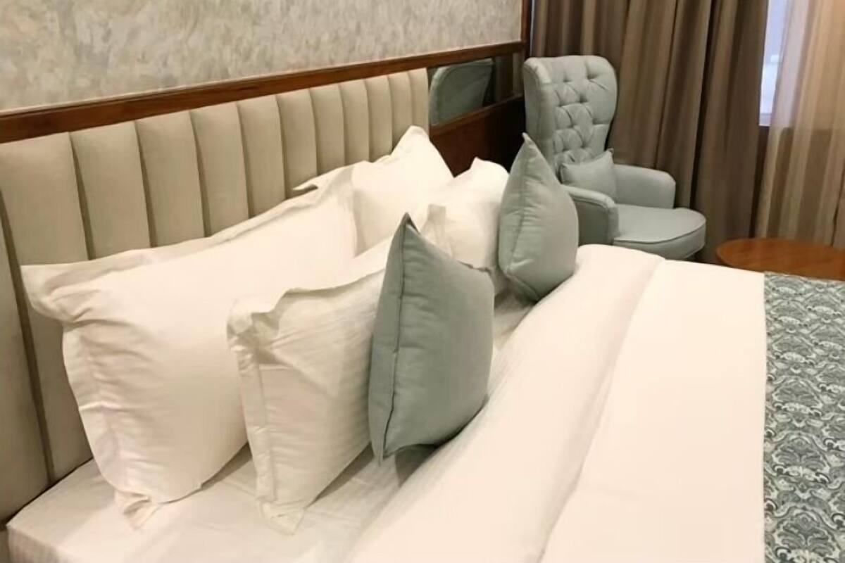 Ein Hotelzimmer mit Bett, Kissen, einem Sessel, einem kleinen Tisch und einem Spiegel.