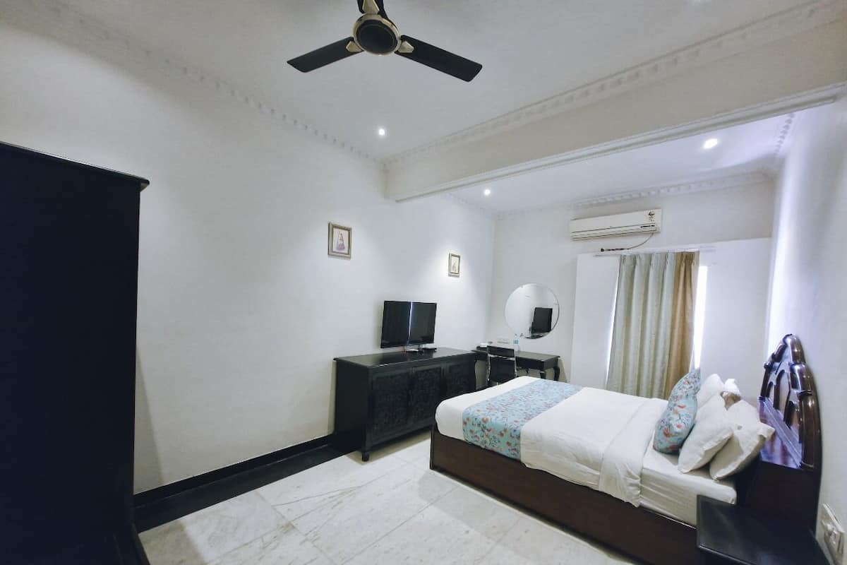 A hotel room with a bed, a dresser, a television, and an air conditioning unit.