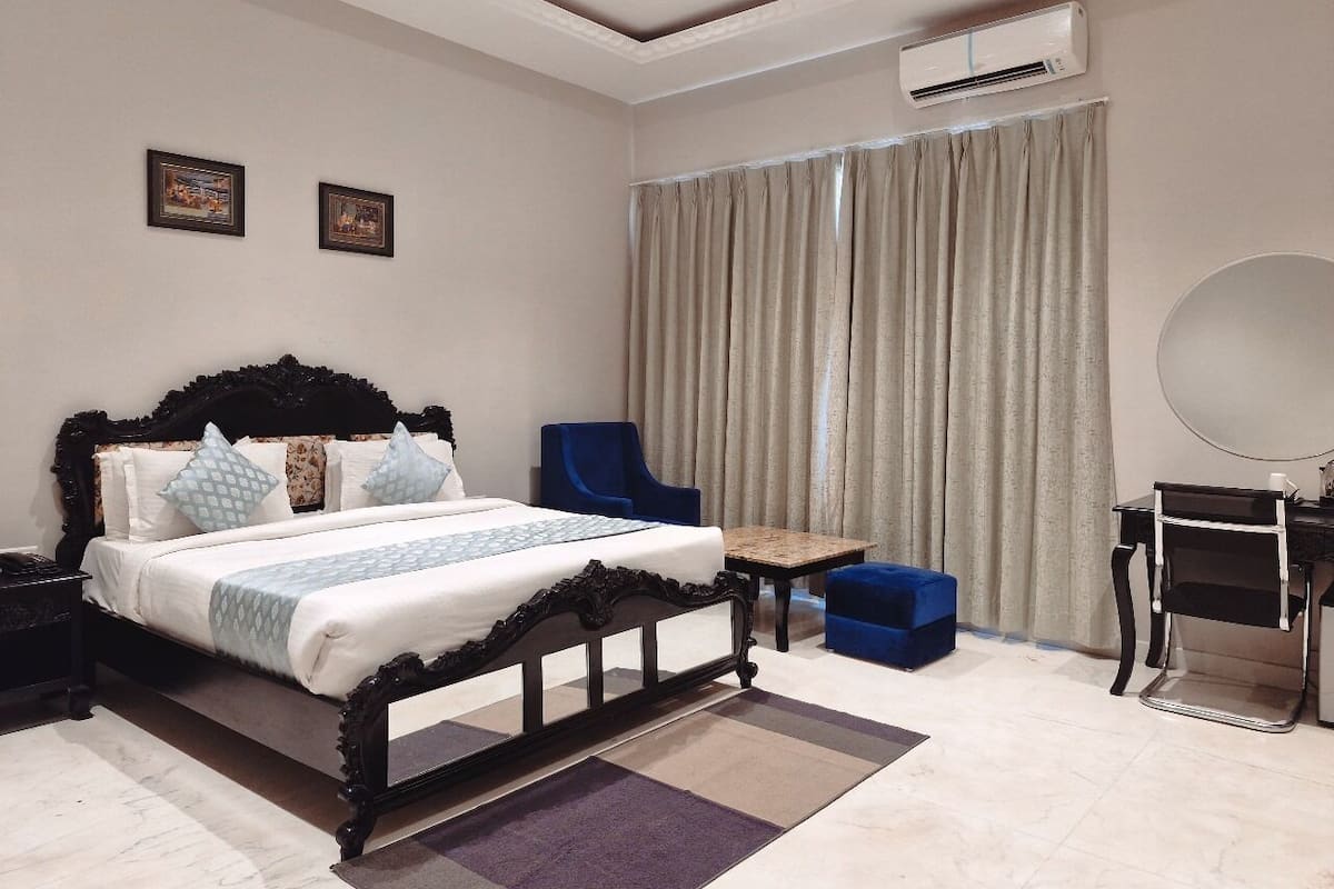 A bedroom with a large bed, a desk, a chair, and an air conditioning unit.