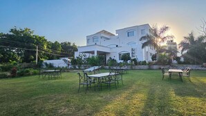 Un edificio moderno y blanco con un amplio espacio exterior que incluye césped y varias mesas y sillas.