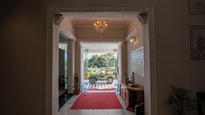 Un pasillo con alfombra roja que lleva a una puerta de vidrio, un candelabro y un piso a cuadros.