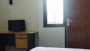 A room with a bed, a desk with a television, a window, and a door. - Homestay Susanto (Pati)