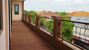 A balcony with a tiled floor, metal railings, and a view of neighboring buildings and greenery. - Homestay Susanto (Pati)
