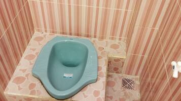 A small, square-shaped toilet with a blue seat and a white label in a room with striped walls and patterned floor tiles.