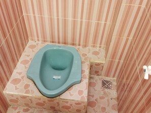 A small, square-shaped toilet with a blue seat and a white label in a room with striped walls and patterned floor tiles. - Homestay Susanto (Pati)
