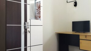 A room with a wooden desk, a television, and a door with a key lock. - Homestay Susanto (Pati)