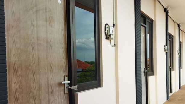 A corridor with wooden flooring, a large wooden door, and multiple windows with black frames. - Homestay Susanto (Pati)