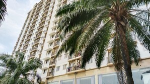 A high-rise building with multiple balconies, large windows, and palm trees. - Amerta Room Apartemen Mutiara by Cocotel (Bekasi)