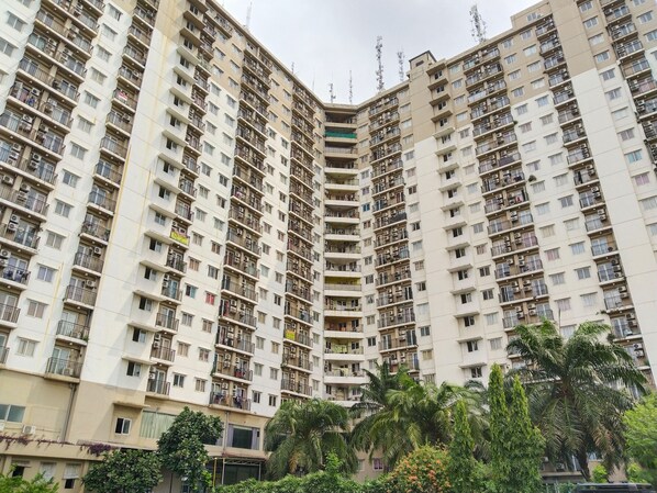 Un edificio residencial de gran altura con múltiples balcones, unidades de aire acondicionado y una entrada porticada.