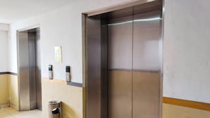A hallway with two elevators, a trash bin, and a wall-mounted intercom. - Amerta Room Apartemen Mutiara by Cocotel (Bekasi)