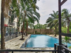Una piscina rodeada de palmeras y un muro de piedra, con un edificio al fondo.