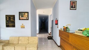 Uma área de recepção de hotel, com balcão, um sofá e um corredor que dá para outros quartos.