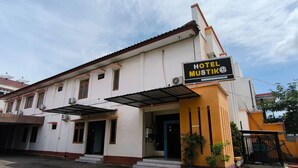 Um hotel chamado "HOTEL MUSTIK" com fachada branca, telhado vermelho e uma placa de identificação.
