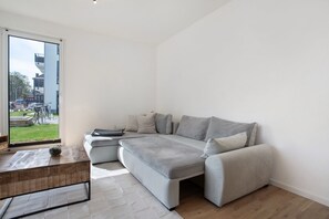 Un salon moderne avec un canapé d’angle, une table basse et une vue sur l’extérieur grâce à une grande fenêtre.