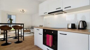 A modern kitchen with white cabinets, a wooden countertop, and a black oven. There are two bar stools and a coffee machine on the counter. - Top Loft Apartment with Private Terrace, Shared Garden, and Wi-Fi (Greifswald)