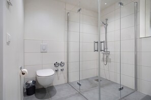 Une salle de bain moderne avec une douche à parois de verre, des toilettes et une poubelle.