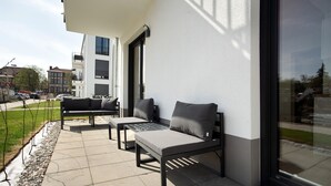 An outdoor seating area with two sofas and a table, a glass door, and a view of the street. - Top Loft Apartment with Private Terrace, Shared Garden, and Wi-Fi (Greifswald)