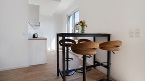 A modern kitchen with a black table and brown bar stools, a vase with flowers on the table, and a window with a view. - Top Loft Apartment with Private Terrace, Shared Garden, and Wi-Fi (Greifswald)