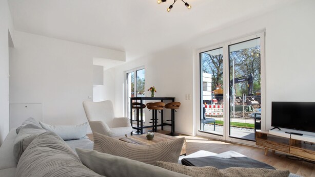 A modern living room with a sofa, a TV, and a dining area with stools. - Top Loft Apartment with Private Terrace, Shared Garden, and Wi-Fi (Greifswald)