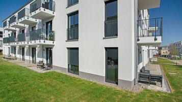 A multi-story residential building with balconies, a grassy lawn, and a clear sky.