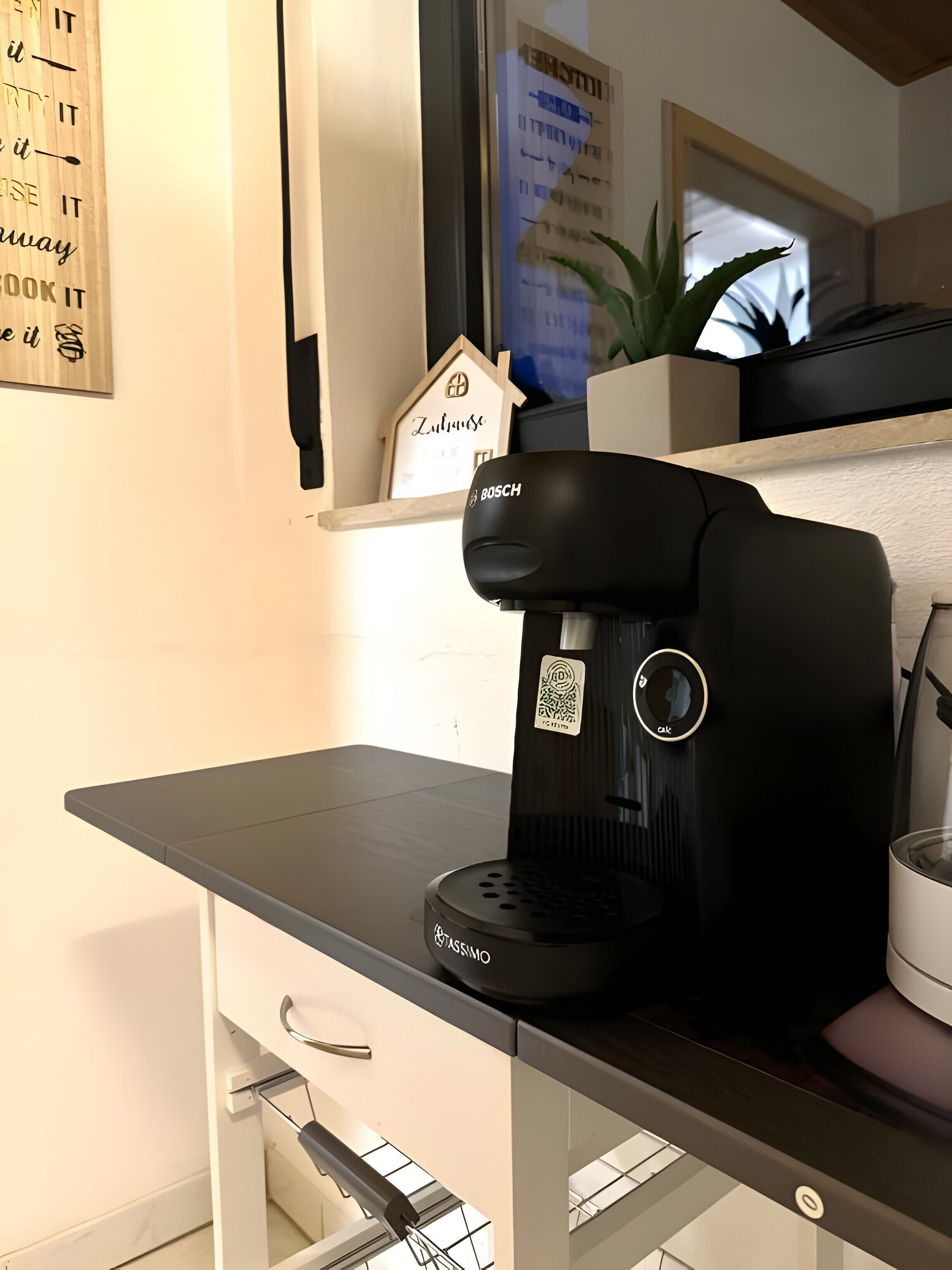 Een keukenhoek met een koffiezetapparaat, een koelkast en een raam met uitzicht.