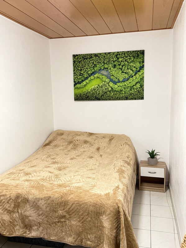 Quarto com cama, mesa de cabeceira com planta e pintura pendurada na parede.