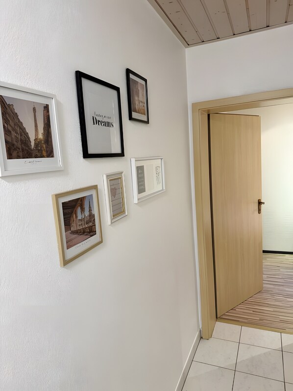 Un couloir avec des tableaux encadrés accrochés au mur, une porte en bois et un sol carrelé.