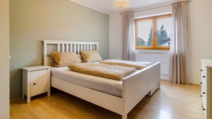 A bedroom with a bed, a nightstand, a dresser, a window with curtains, and a hanging light fixture. - Apartment 'Donauliebe' with Private Terrace, Shared Garden and Wi-Fi (Sigmaringen)