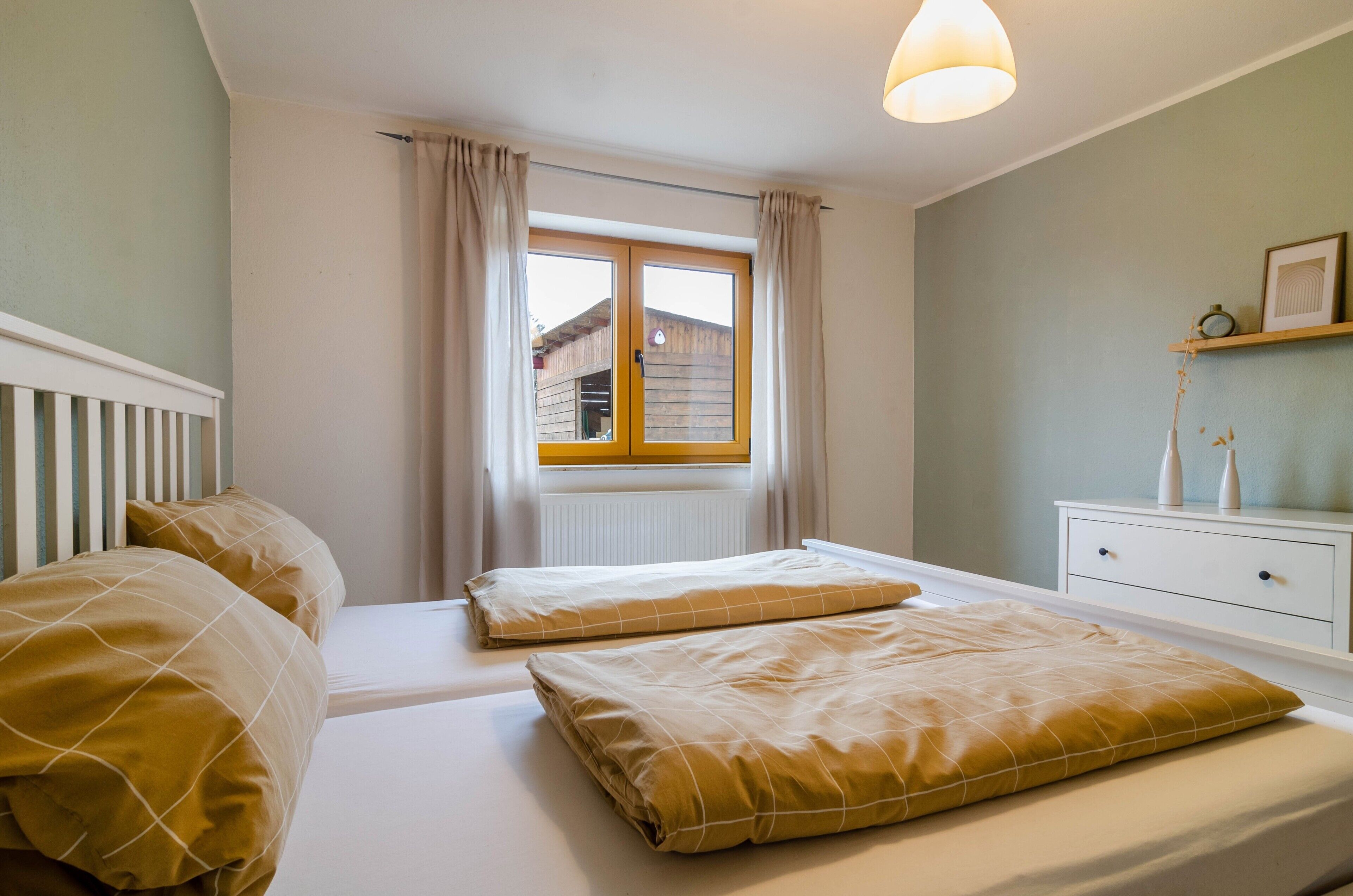 Una camera da letto con due letti, una finestra con tende, un comodino con una lampada e uno scaffale con oggetti decorativi.