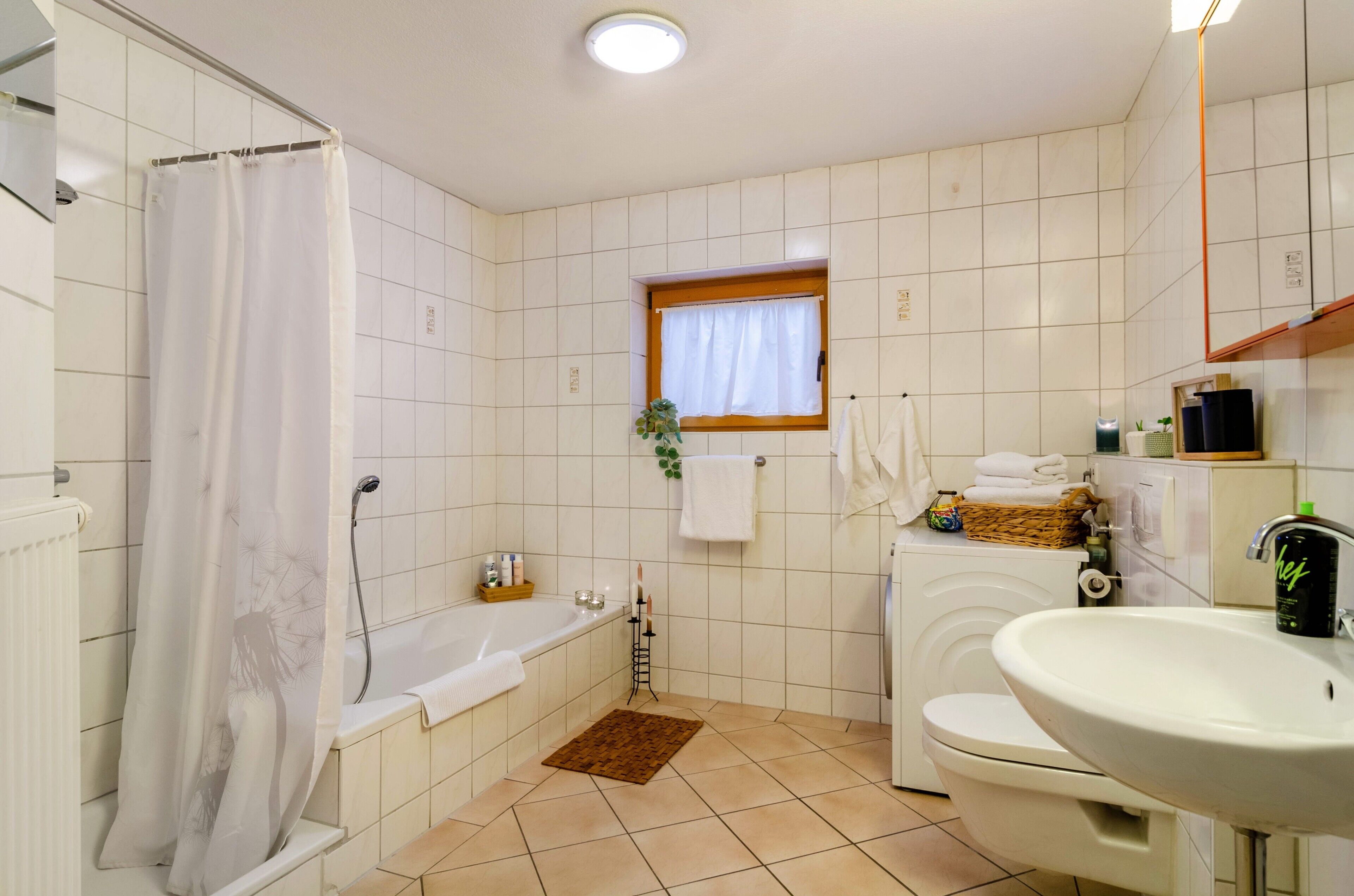 Ein Badezimmer mit Badewanne, Toilette, Waschbecken und einem Fenster mit Vorhang.