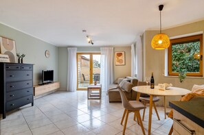 Un salon moderne comprenant un téléviseur, un canapé, une table à manger et donnant sur un espace extérieur grâce à une porte vitrée.