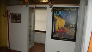 Een kamer met een poster van Vincent van Goghs 'Café de Nuit', een glazen deur, een rode kapstok en een klein houten krukje.