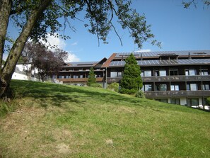 Um edifício com várias varandas, painéis solares no telhado e um declive gramado.